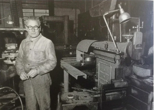 jean Prouvé dans son atelier devant une machine sur laquelle est montée une lampe Eclair de Emile Eugene Houillon